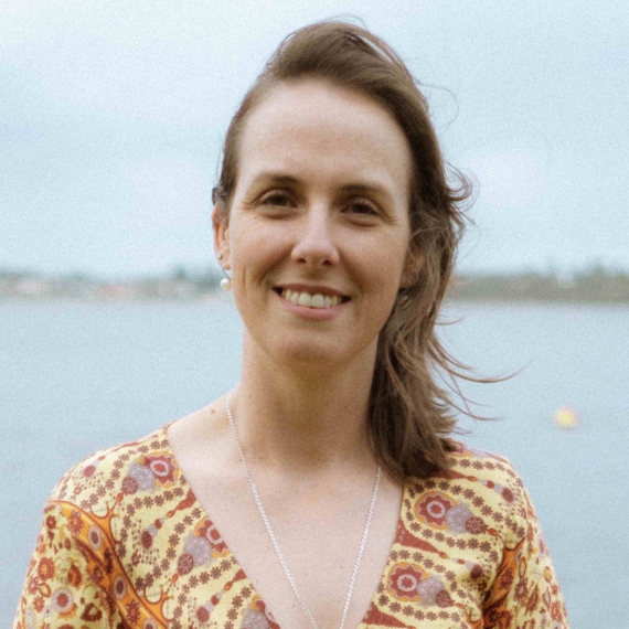 Naturopath Debbie Wilkinson - standing in front of a body of water. Wind is blowing her hair. she is early 40's, with brown hair, smiling