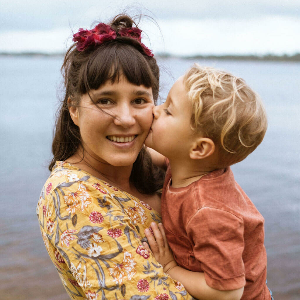 Young mother smiling whilst being kissed on cheek by her toddler.