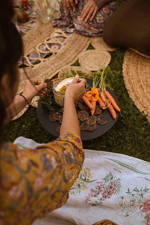 Earthy picnic, platter with carrots and cashew cheese and someone putting some cashew cheese on a cracker