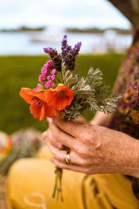 A woman's hand holding a small bouquet of flowers, lavender, orange nasturtium and a tiny snail on the flower