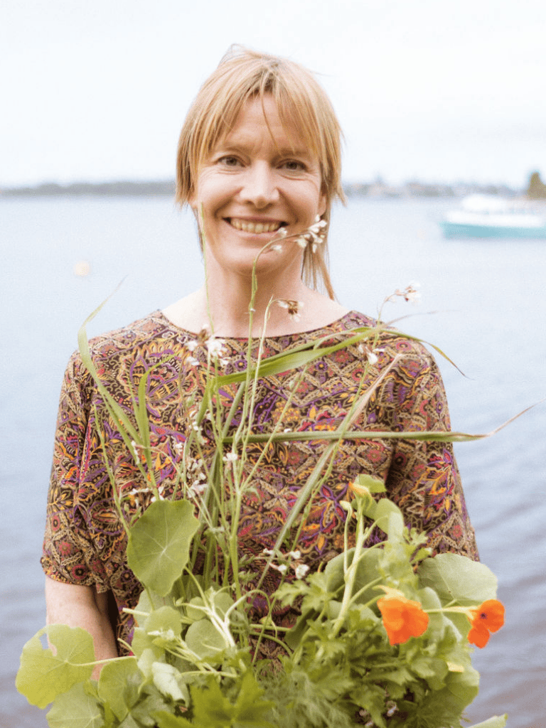 Middle aged woman holding a bouquet of leafy greens from the garden, standing in front of the river