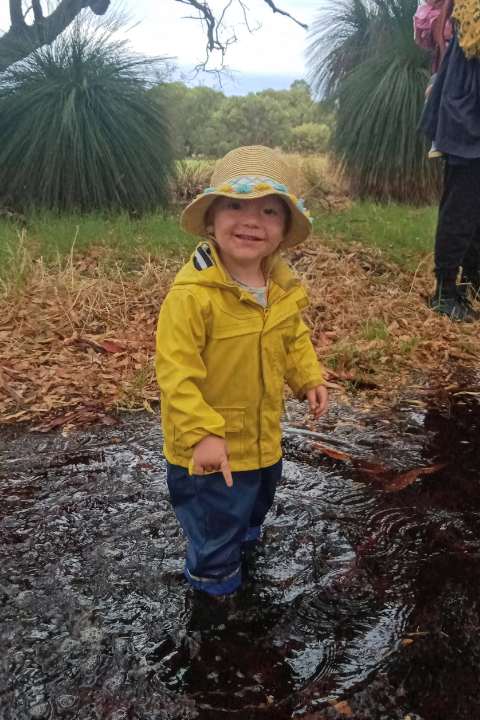 3 year old boy in yellow rain jacket standing in a big puddle of water on a rainy day
