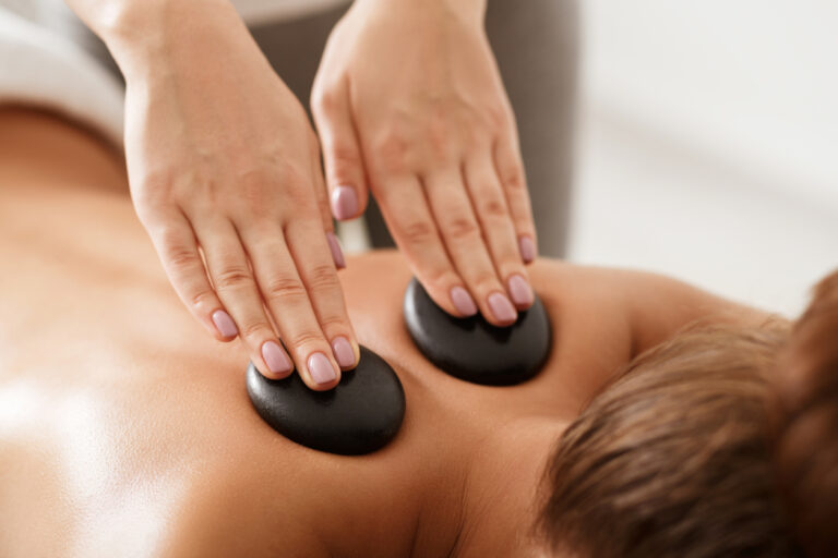 Relaxed woman getting hot stones massage, masseur placing stones on back, closeup