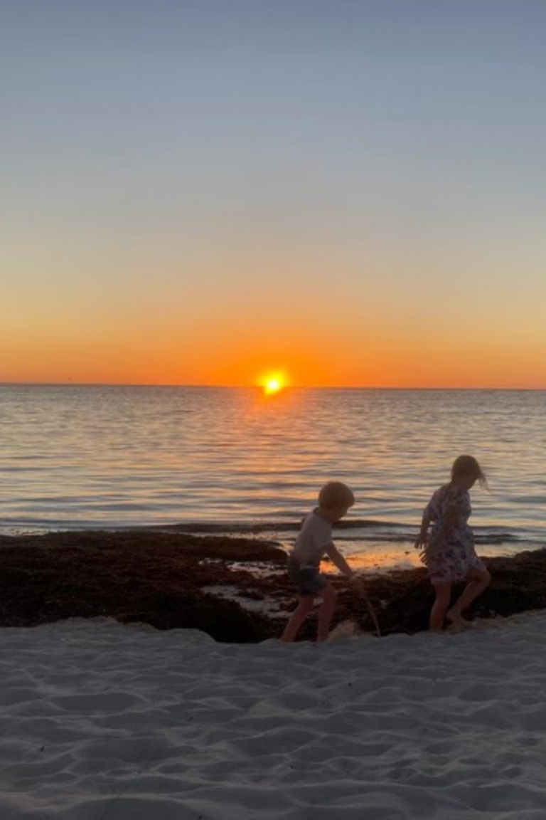 A sunset on the beach with two children walking along the shore line almost like silhouettes