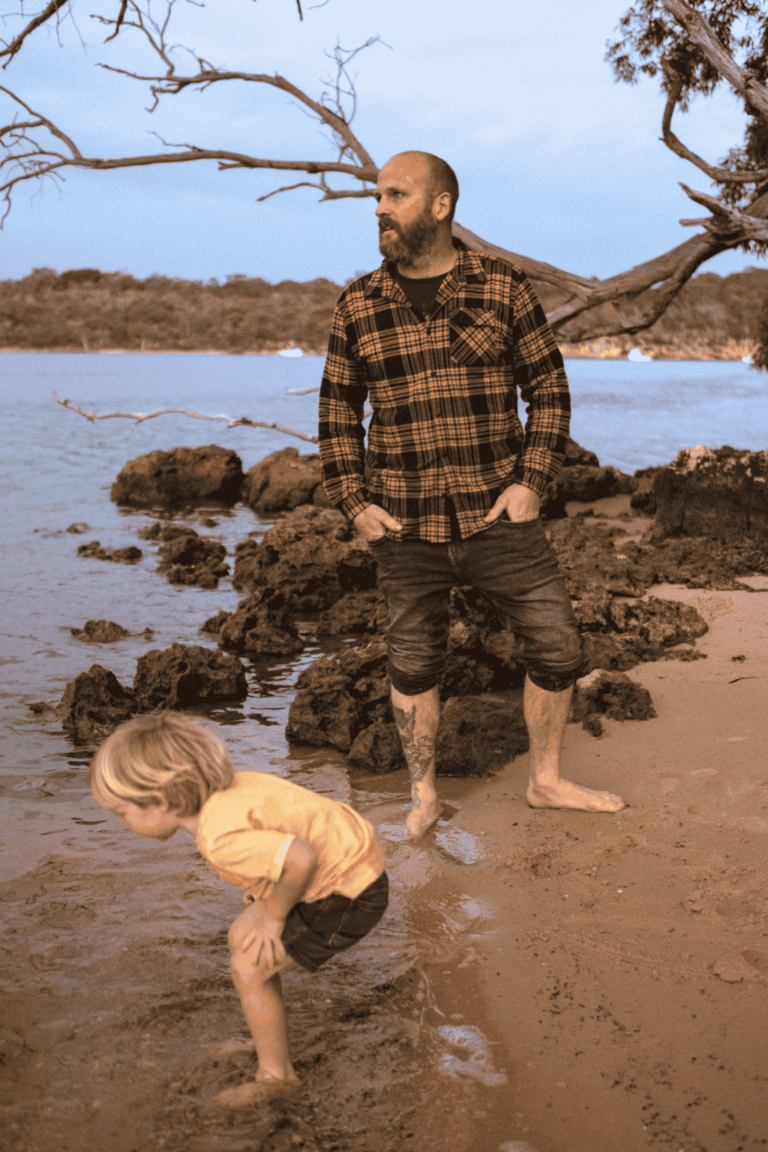 Father on the rivers edge, looking out to the river son 5 year old, bent over playing with the water