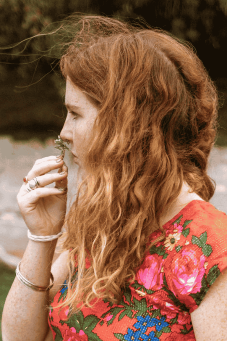 Young woman with wavy rd hair sniffing a flower